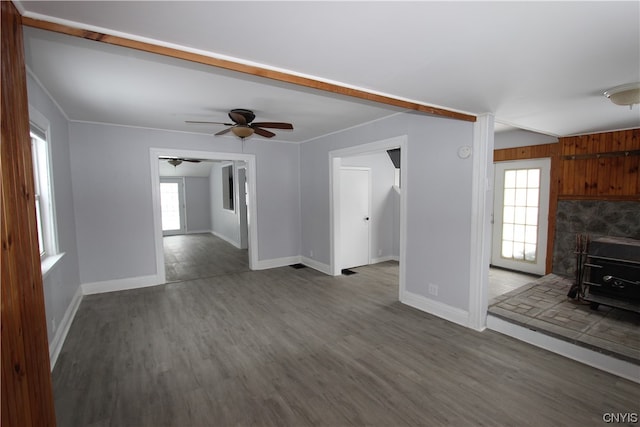 unfurnished living room featuring ceiling fan, a wood stove, plenty of natural light, and dark hardwood / wood-style floors