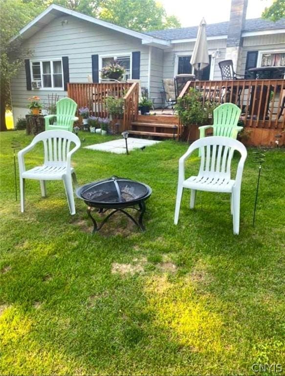 back of property with a wooden deck, a fire pit, and a lawn