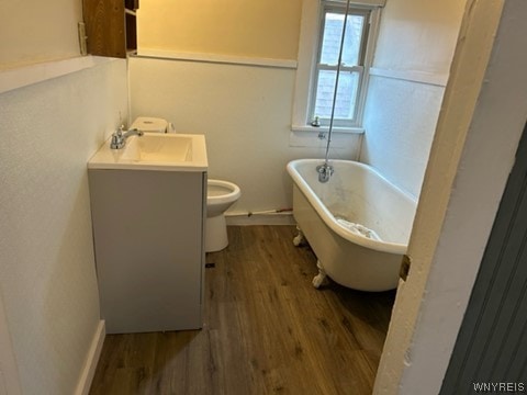 bathroom with toilet, hardwood / wood-style floors, vanity, and a bath to relax in