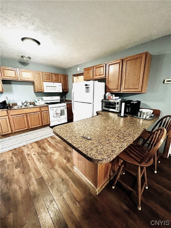 kitchen featuring kitchen peninsula, dark hardwood / wood-style flooring, a breakfast bar, a textured ceiling, and white appliances