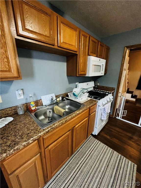 kitchen with white appliances, sink, a textured ceiling, dark stone counters, and dark wood-type flooring