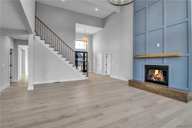 unfurnished living room featuring light hardwood / wood-style flooring, a chandelier, and a high ceiling