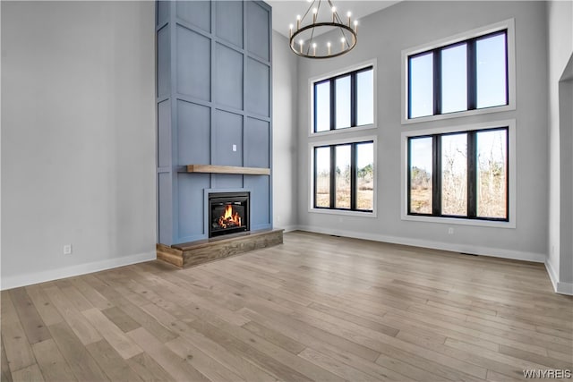 unfurnished living room featuring a towering ceiling, a chandelier, and light hardwood / wood-style floors