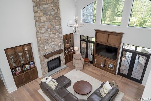 living room featuring a stone fireplace, a notable chandelier, plenty of natural light, and light hardwood / wood-style flooring