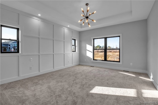 spare room with light colored carpet, a raised ceiling, and an inviting chandelier