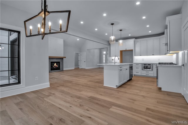 kitchen featuring an island with sink, white cabinets, decorative light fixtures, a notable chandelier, and light wood-type flooring