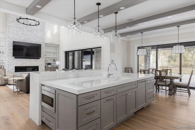 kitchen featuring decorative light fixtures, beamed ceiling, a stone fireplace, light hardwood / wood-style flooring, and sink