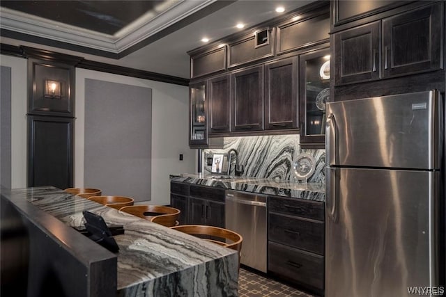 kitchen featuring dark stone counters, stainless steel appliances, backsplash, dark brown cabinets, and crown molding