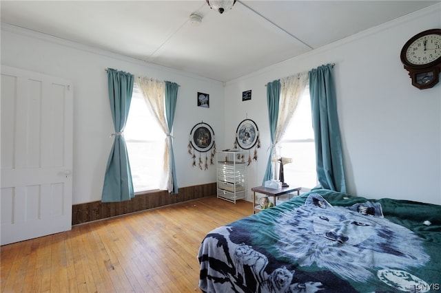 bedroom with ornamental molding, light wood-type flooring, multiple windows, and wooden walls