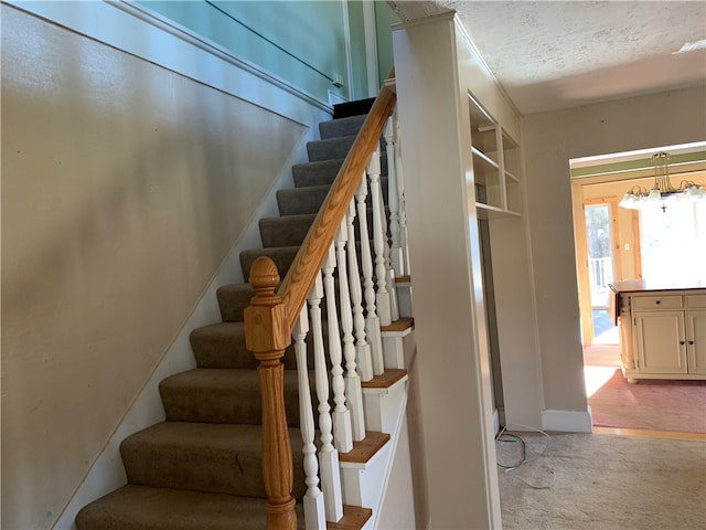 staircase with a notable chandelier, light colored carpet, and a textured ceiling