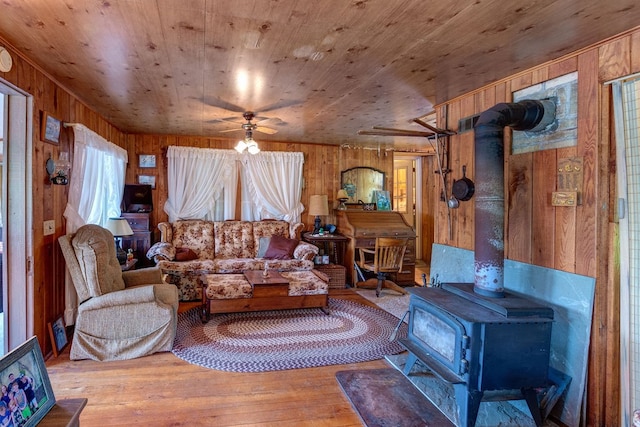 living room with hardwood / wood-style flooring, ceiling fan, wood walls, and a wood stove