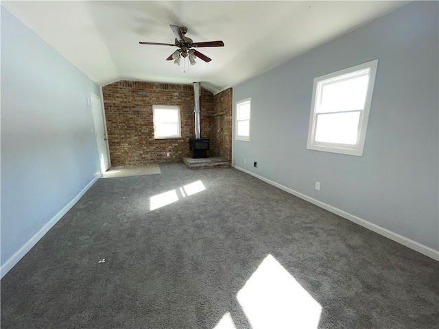 unfurnished living room with lofted ceiling, a wood stove, dark carpet, ceiling fan, and brick wall