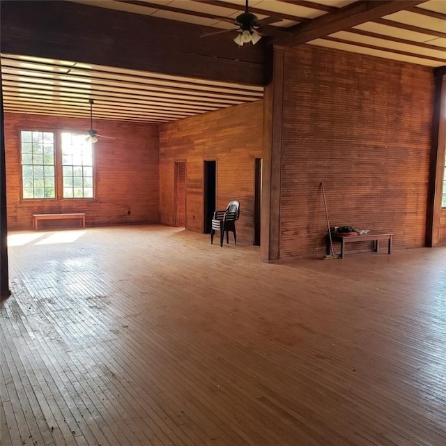 empty room with ceiling fan, wooden walls, and hardwood / wood-style floors