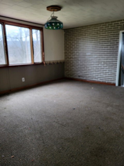 unfurnished room featuring brick wall and carpet floors