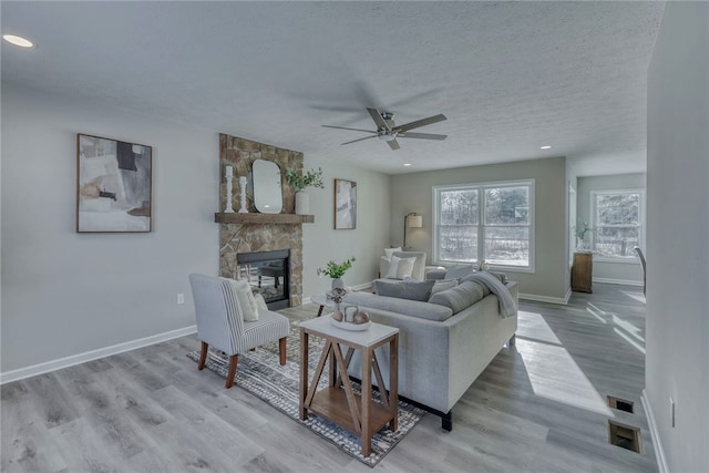 living room featuring light hardwood / wood-style floors, a textured ceiling, a fireplace, and ceiling fan