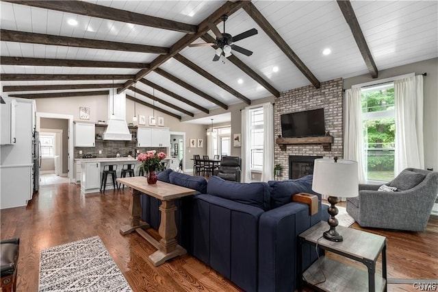 living room featuring ceiling fan, a brick fireplace, vaulted ceiling with beams, wood ceiling, and dark hardwood / wood-style flooring