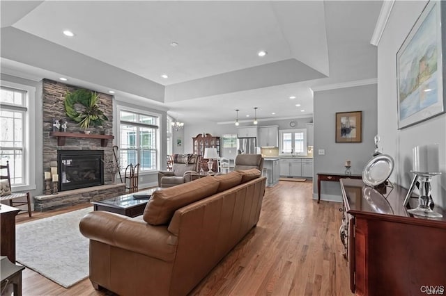 living room featuring ornamental molding, a raised ceiling, a fireplace, and light hardwood / wood-style flooring