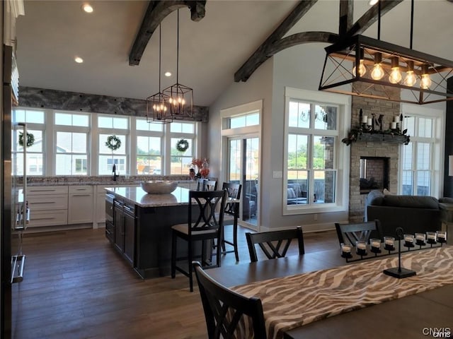 kitchen with a center island, white cabinetry, a fireplace, light stone counters, and beam ceiling