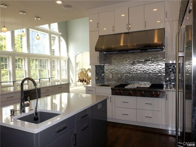 kitchen with white cabinetry, decorative backsplash, hanging light fixtures, light stone counters, and sink