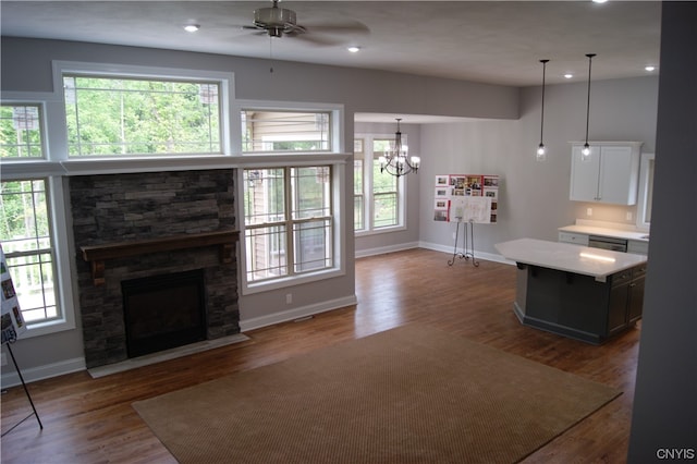 unfurnished living room with ceiling fan with notable chandelier, dark hardwood / wood-style floors, and a stone fireplace