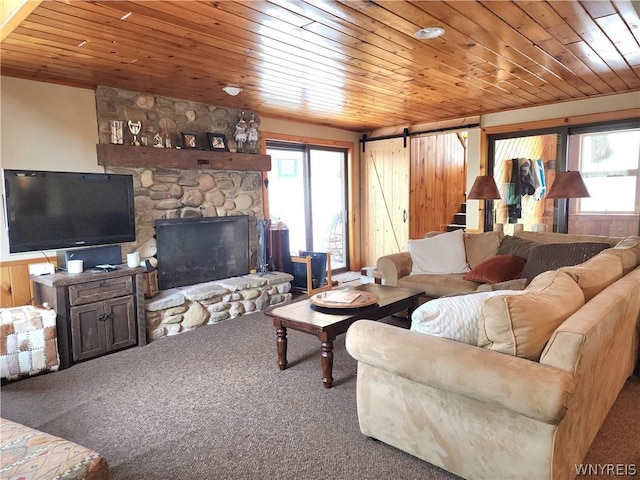 carpeted living room with a stone fireplace, wooden ceiling, and a barn door