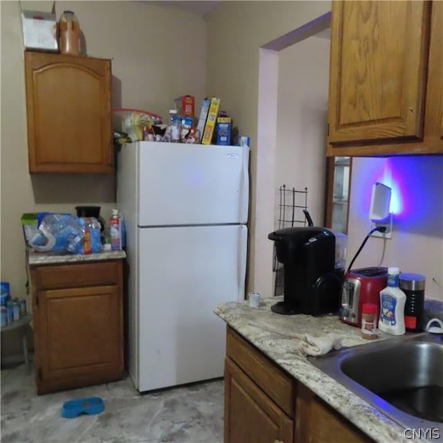 kitchen with light tile floors, light stone counters, sink, and white refrigerator