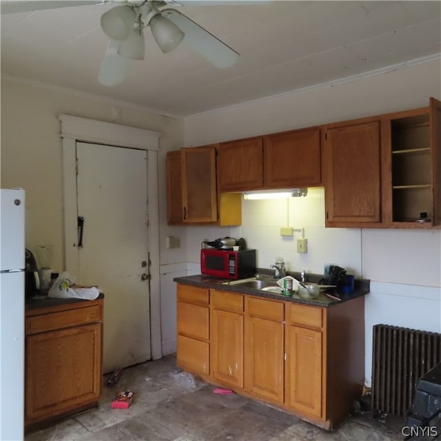 kitchen featuring white refrigerator, ceiling fan, radiator heating unit, and sink