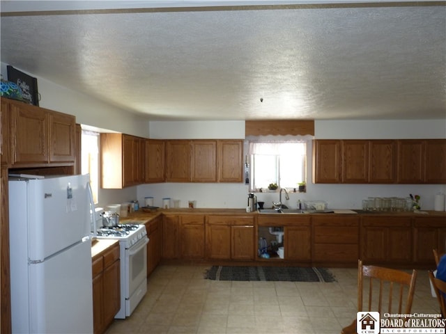 kitchen with white appliances, sink, a textured ceiling, and light tile floors