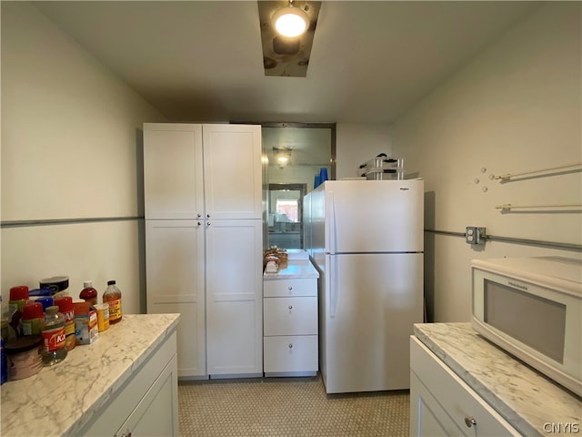 kitchen featuring light stone counters, white appliances, light tile floors, and white cabinetry