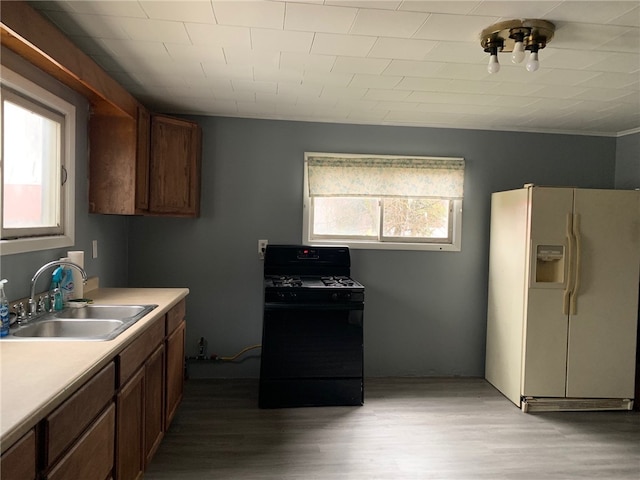 kitchen featuring white refrigerator with ice dispenser, black range with gas stovetop, sink, and hardwood / wood-style floors