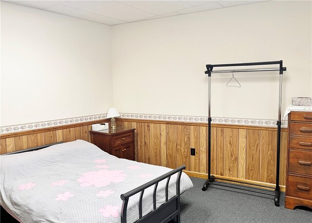 bedroom featuring carpet floors, wooden walls, and a paneled ceiling