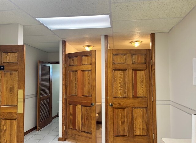 hall with a paneled ceiling and light tile floors