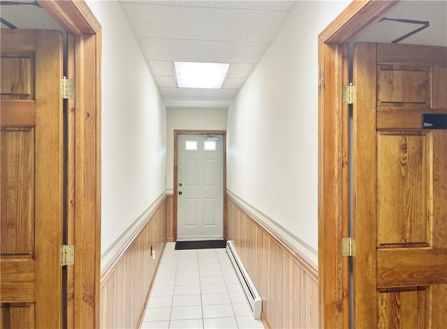 hall featuring a drop ceiling, a baseboard heating unit, and light tile floors