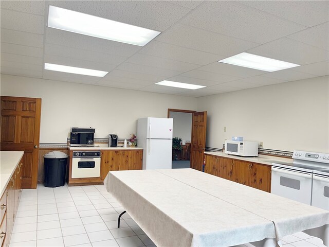 kitchen featuring white appliances, light tile floors, and a paneled ceiling