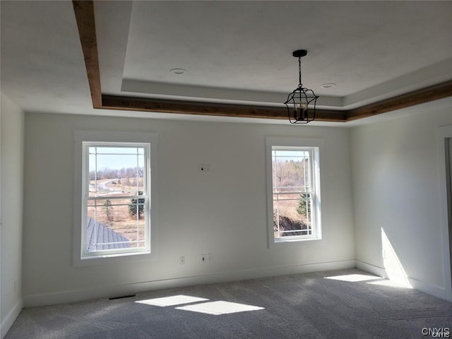 carpeted empty room featuring a notable chandelier and a raised ceiling