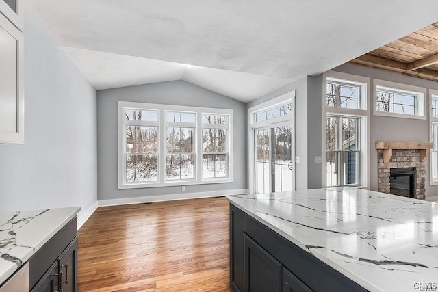 kitchen with wood ceiling, a stone fireplace, vaulted ceiling, light hardwood / wood-style floors, and light stone counters