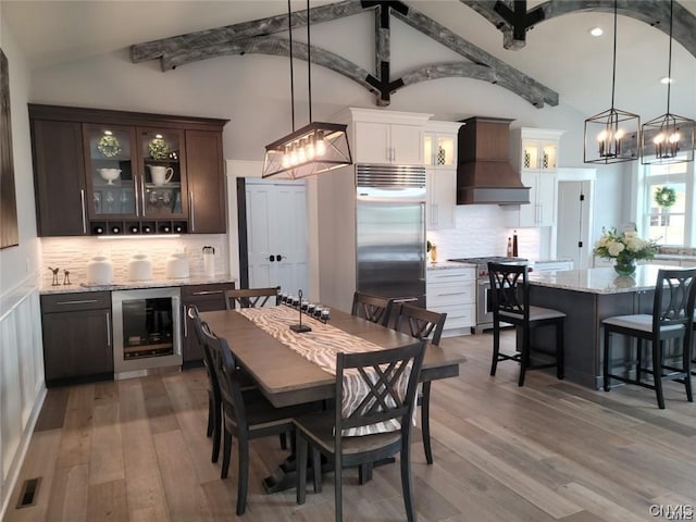 dining room with light hardwood / wood-style floors, beverage cooler, and vaulted ceiling with beams