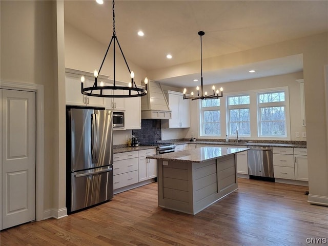 kitchen featuring light stone counters, a center island, stainless steel appliances, custom range hood, and white cabinetry