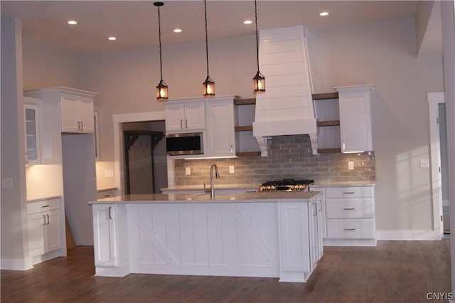 kitchen featuring white cabinets, decorative light fixtures, a kitchen island with sink, and stainless steel microwave