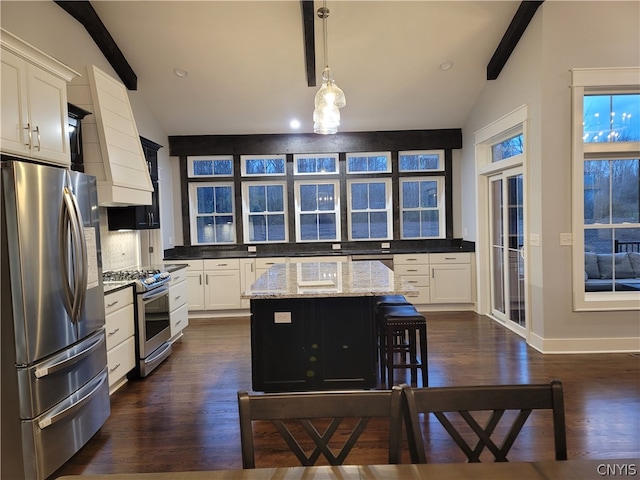 kitchen featuring light stone countertops, lofted ceiling with beams, a center island, decorative light fixtures, and appliances with stainless steel finishes