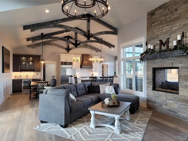 living room featuring wine cooler, a fireplace, light hardwood / wood-style flooring, high vaulted ceiling, and a chandelier