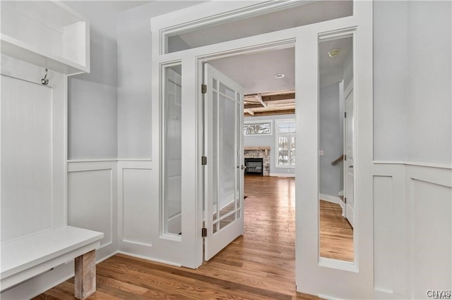 mudroom with coffered ceiling, beam ceiling, hardwood / wood-style floors, and a stone fireplace