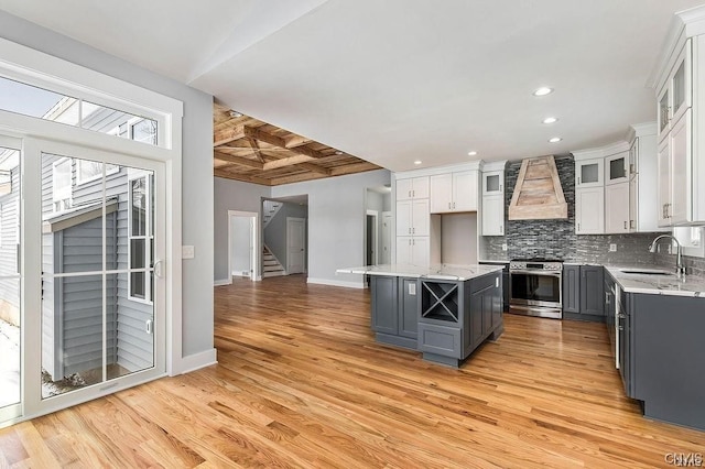 kitchen with premium range hood, gray cabinets, stainless steel stove, a kitchen island, and sink