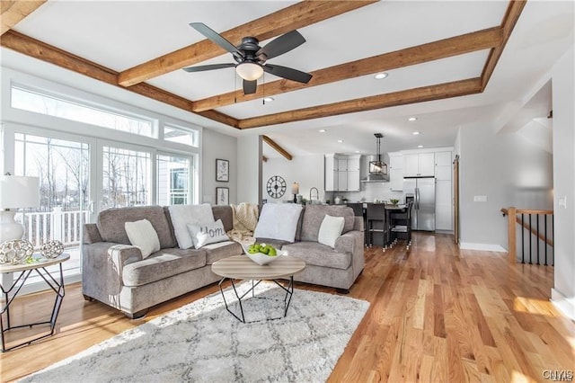 living room with ceiling fan, light wood-type flooring, and beamed ceiling