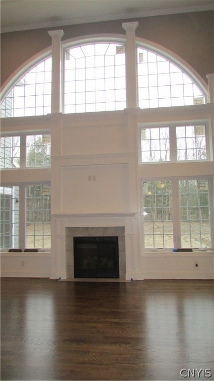 unfurnished living room featuring a high ceiling, dark hardwood / wood-style floors, and a tiled fireplace