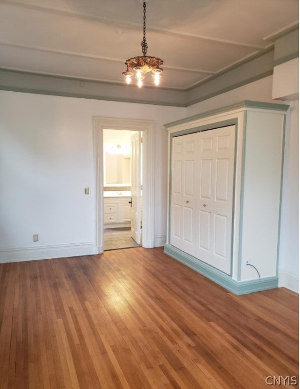 unfurnished bedroom featuring an inviting chandelier, wood-type flooring, and a closet