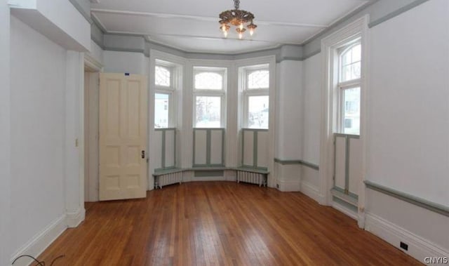 empty room with a chandelier, radiator heating unit, and dark hardwood / wood-style flooring