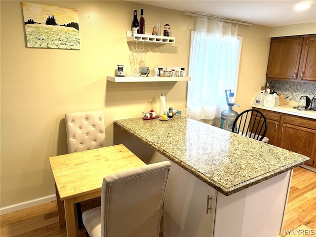 kitchen with light stone counters, tasteful backsplash, and light wood-type flooring