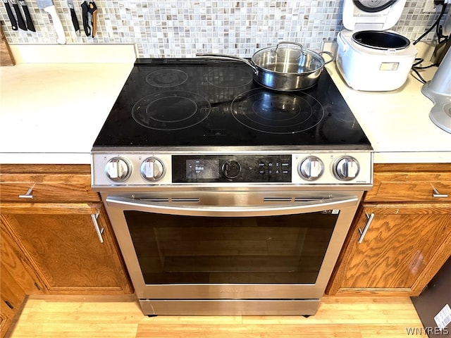 details featuring stainless steel electric range, backsplash, and light hardwood / wood-style flooring