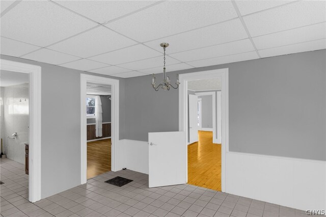 spare room featuring a chandelier, tile patterned flooring, and a drop ceiling